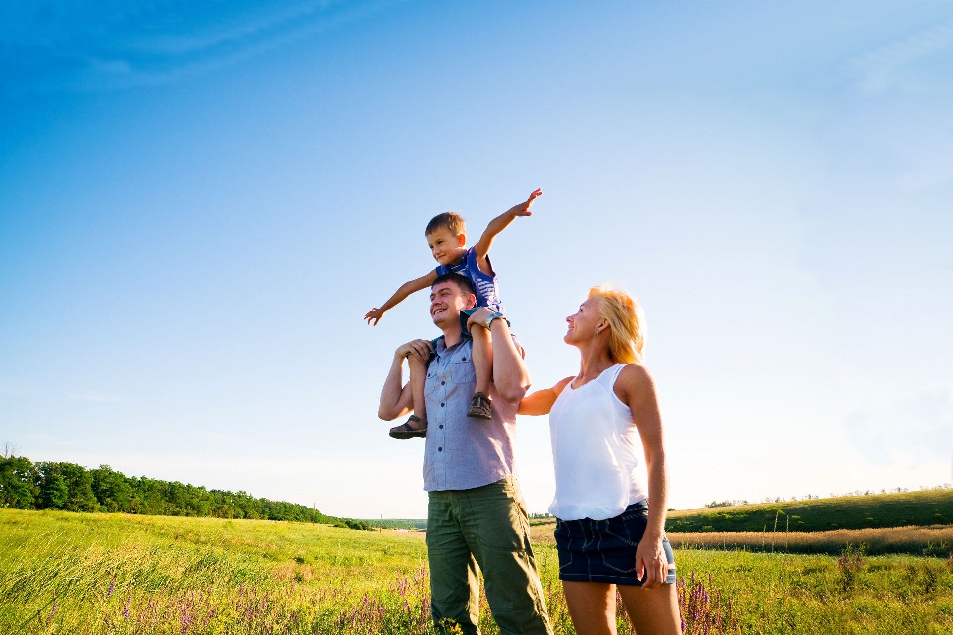 Family standing in a green field with the son on the father's shoulders holding his arms out