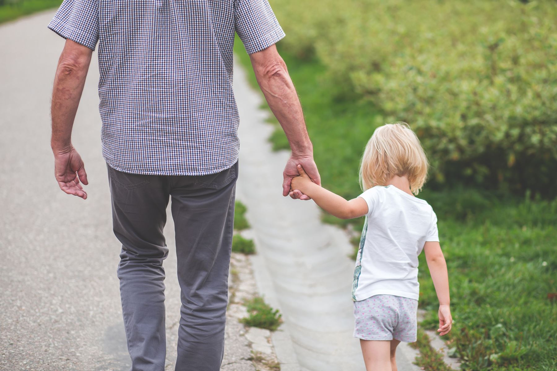 Father holding daughters hand walking away from the camera down a dirt road